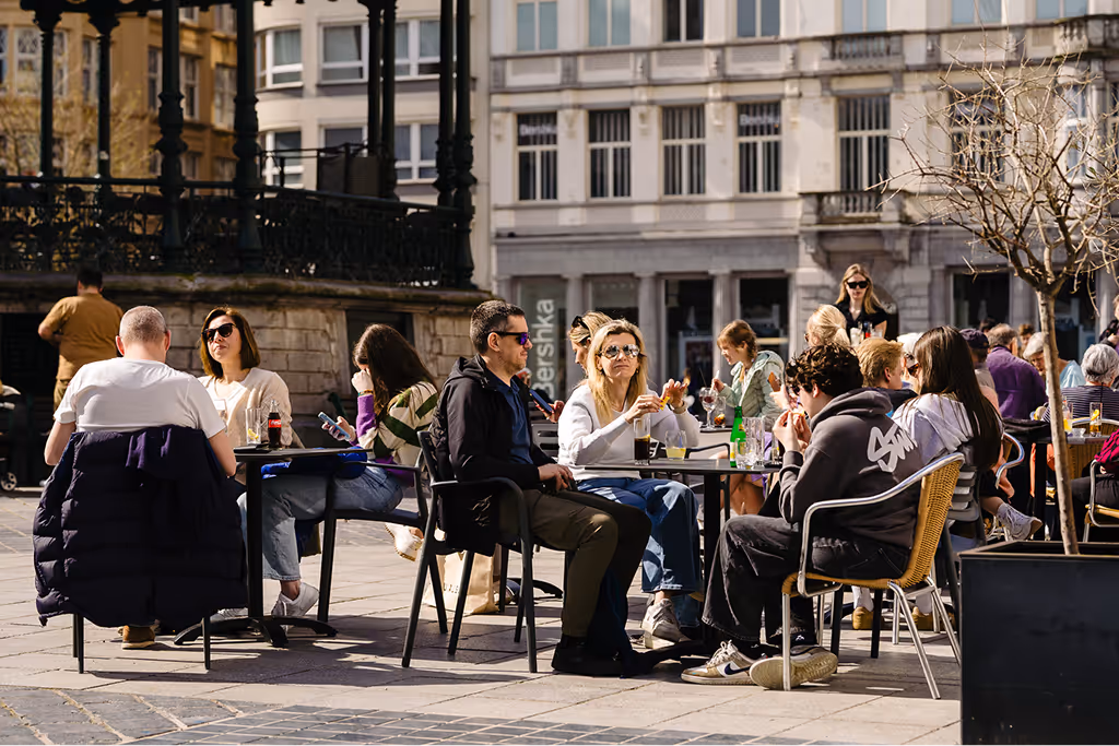 People sitting and dining at outdoor cafe tables on a sunny day in a city square.